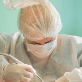 Pessoa com roupa branca médica e trabalhando com instrumento na mão.
